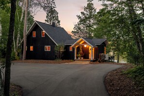 Une cabane à deux étages, dotée d’un toit à forte pente, d’un porche à l’avant et d’une allée menant à l’entrée.