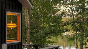 A cabin with a wooden deck overlooking a calm lake, surrounded by trees.