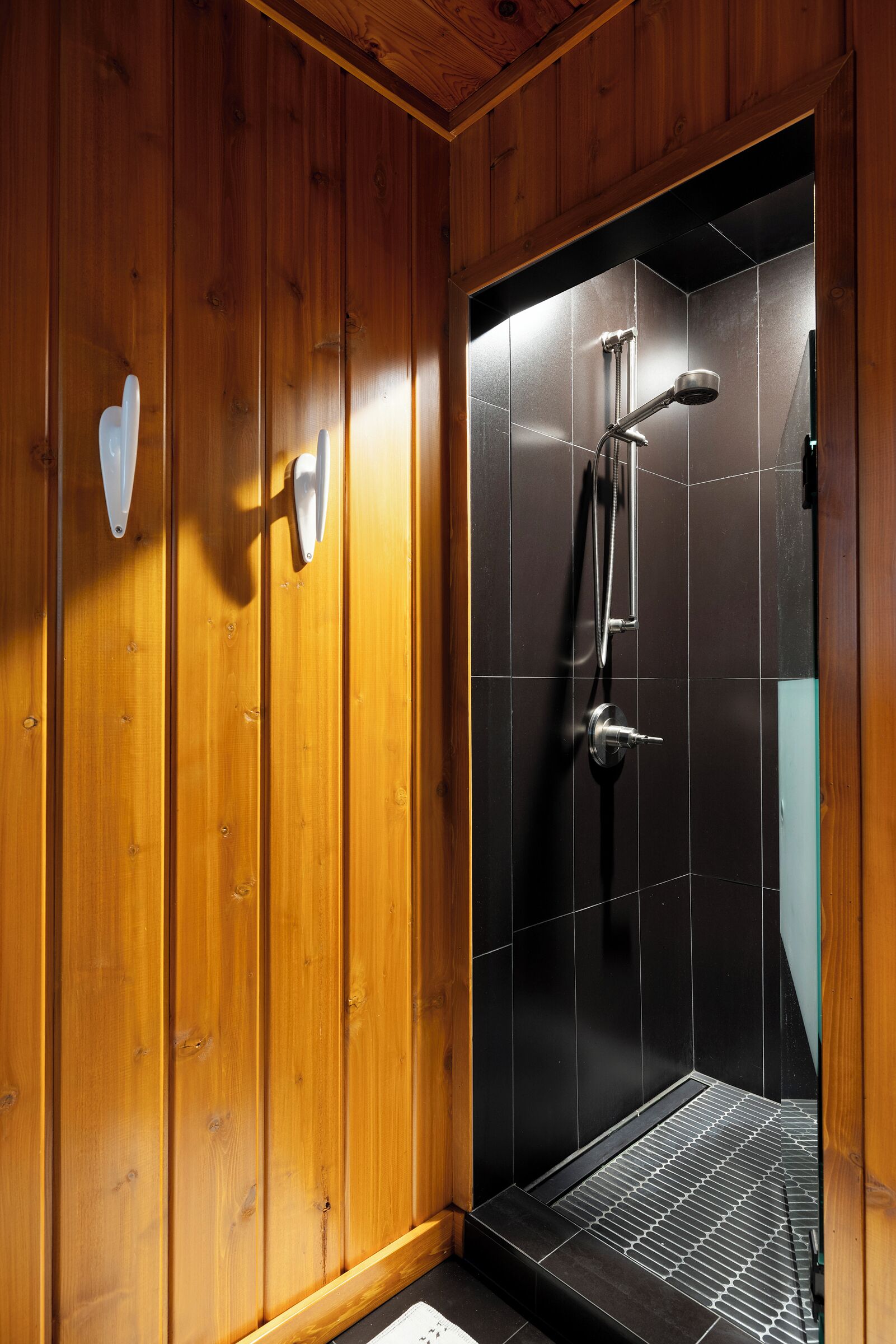 A wooden interior with a shower area featuring a black tiled wall and a metal shower head.