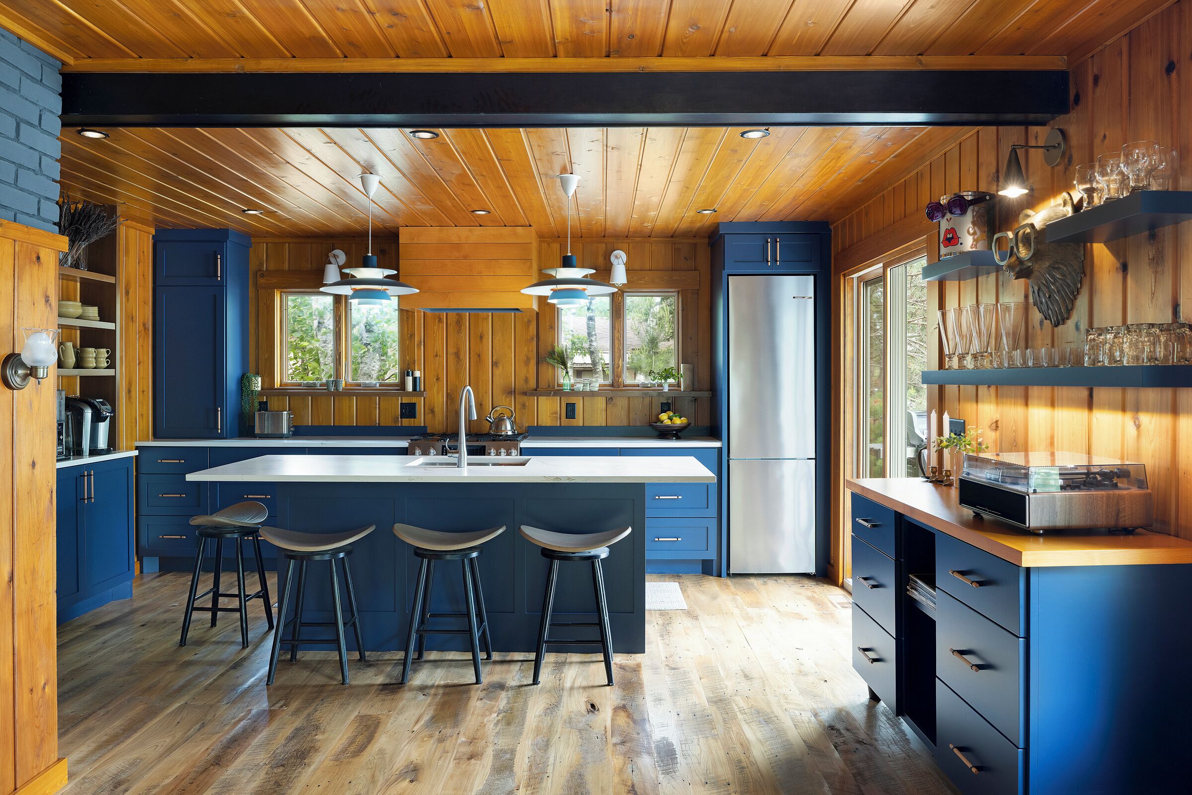 A modern kitchen with a central island, bar stools, and a large window.