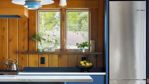 A modern kitchen with wooden paneling, a stainless steel refrigerator, a double sink, and a bar stool.