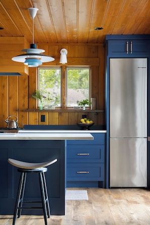 Eine moderne Küche mit Holzwandverkleidung, einem Edelstahlkühlschrank, einer Spüle mit zwei Becken und einem Barhocker.