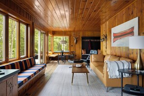 Interior acogedor de una cabaña con techo de madera, un sofá, una mesa de comedor y una chimenea.