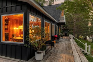 A cabin with large windows, a wooden deck, and outdoor seating.