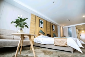 Ett modernt hotellrum med en säng, ett litet runt bord med en växt, en soffa och en väggmonterad TV.