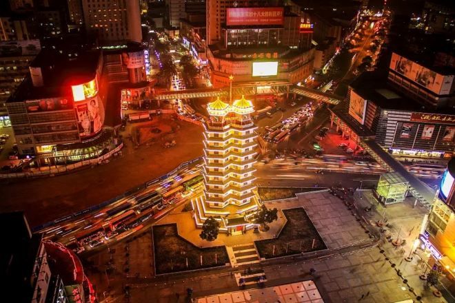 A multi-story building with a central tower, surrounded by a busy urban street at night.