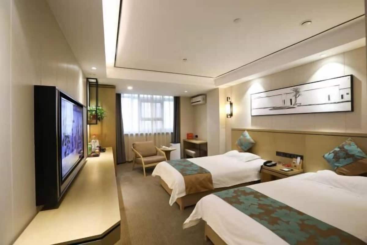 Habitación de hotel con dos camas, televisión, escritorio, silla y ventana con cortinas.