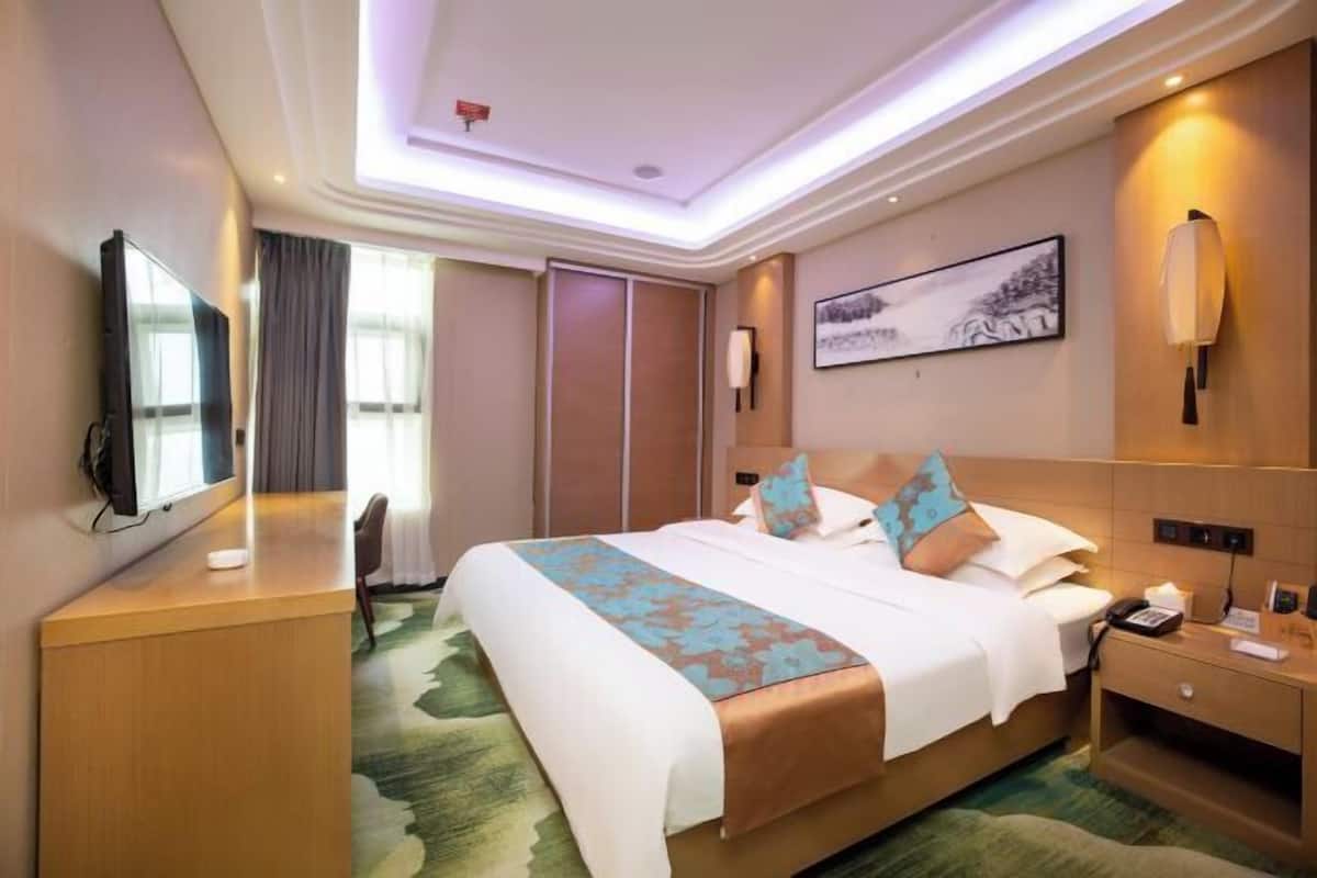 Una habitación de hotel con cama, mesita de noche, lámpara, una obra de arte y televisor.