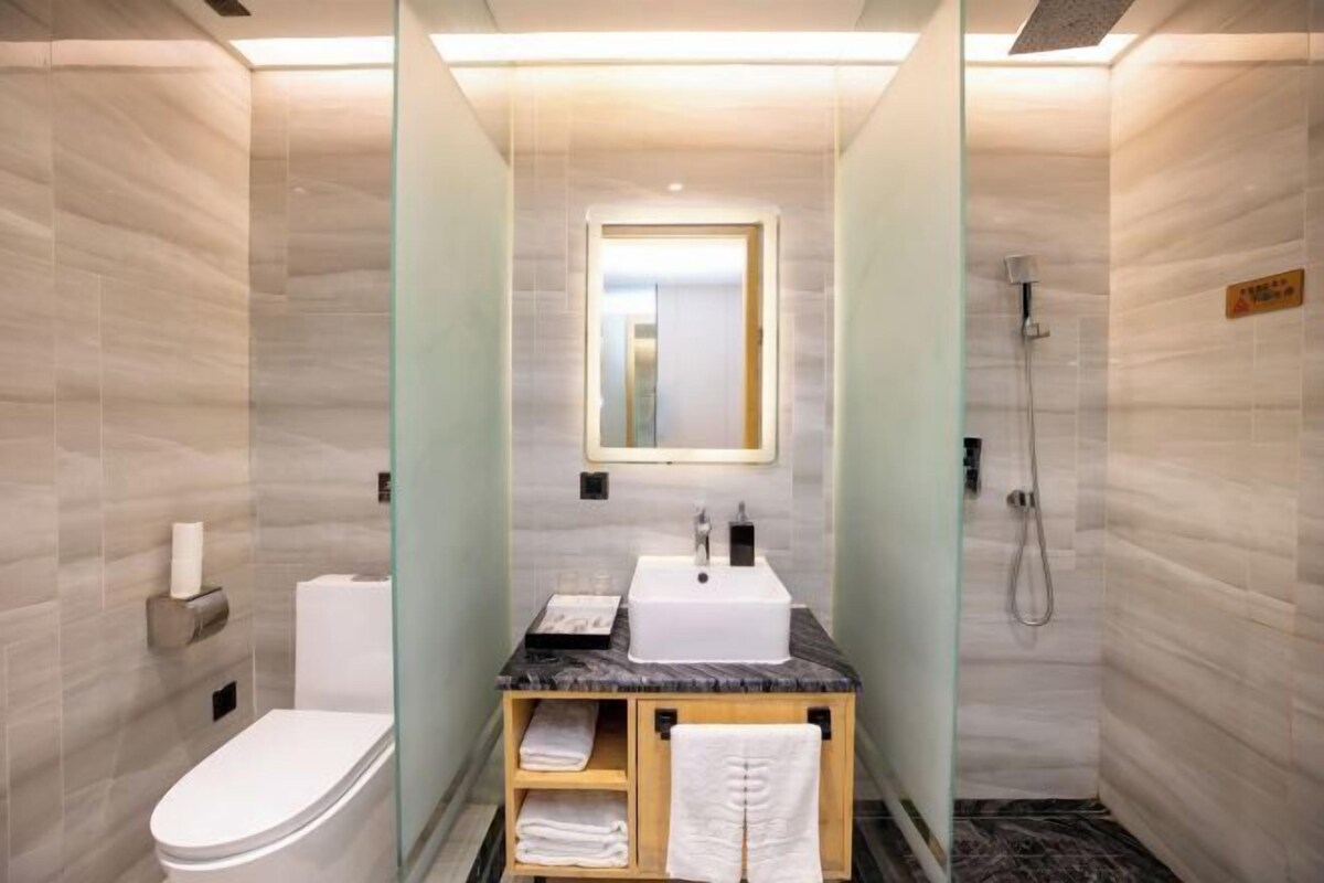 Un baño moderno y compacto con lavamanos de mármol, inodoro y ducha con mampara de vidrio.