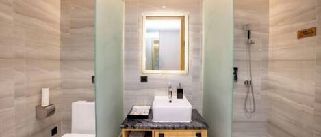 Een compacte, moderne badkamer met een marmeren wastafel, toilet en een douche met glazen wand.
