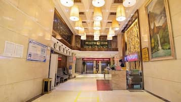 A hotel lobby with a reception desk, seating area, and a large painting on the wall.