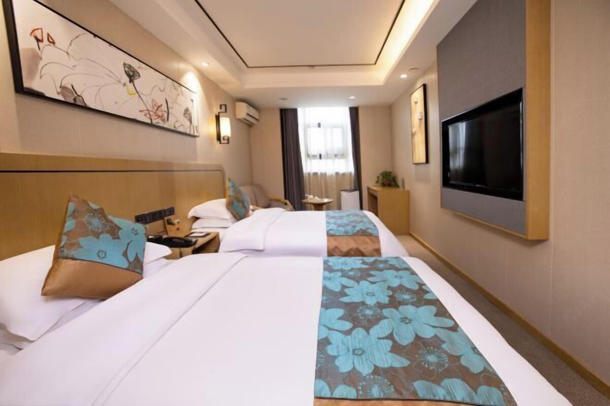 Habitación de hotel con dos camas, un televisor de pantalla plana, obras de arte en las paredes y un ventanal con cortinas.