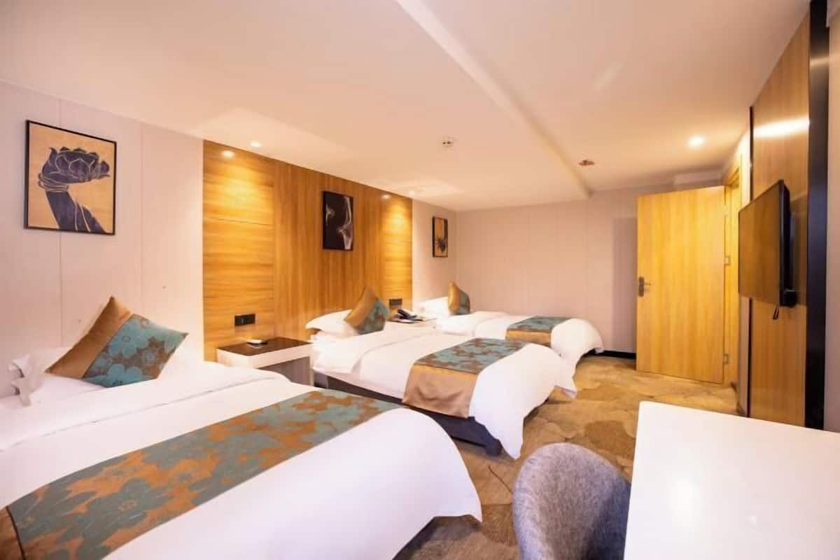 Una habitación de hotel con tres camas, un panel de pared de madera, un televisor de pantalla plana y un escritorio.