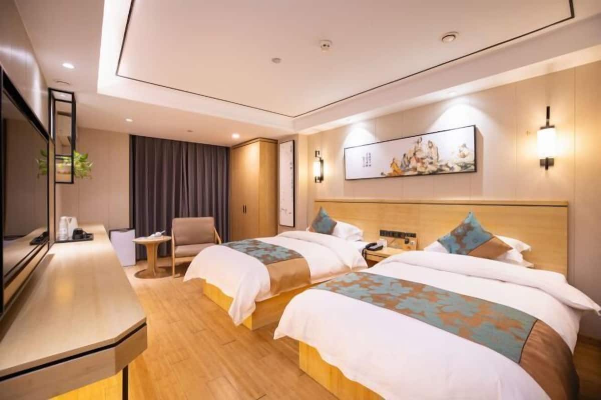 Habitación de hotel con dos camas, un escritorio, una silla y un televisor.
