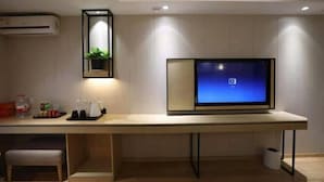 Un salon moderne avec un téléviseur à écran plat fixé au mur, une petite table ornée d’une plante et un banc.