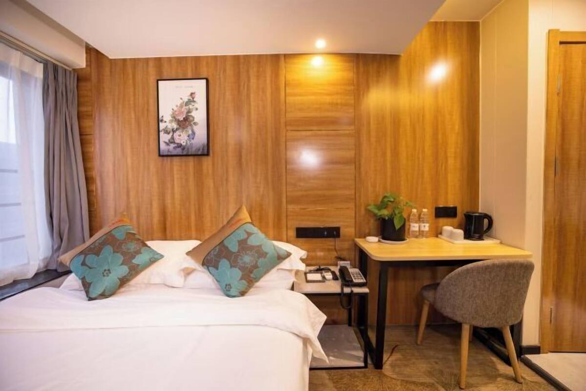 Habitación de hotel con cama, escritorio, silla, teléfono y una mesita con una planta y cafetera.