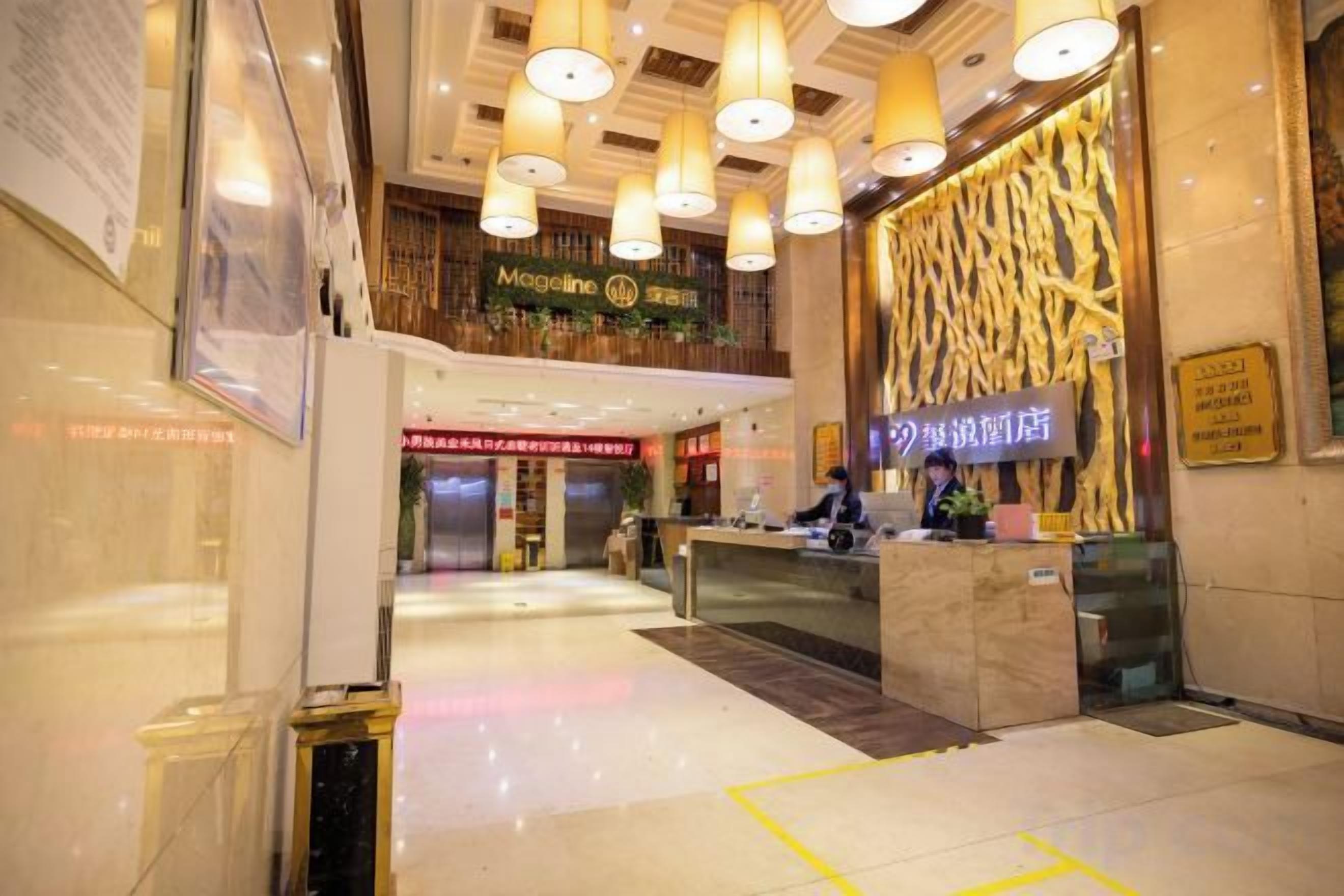 Un vestíbulo de hotel con mostrador de recepción, una escalera y un letrero para el restaurante 'Magaline'.