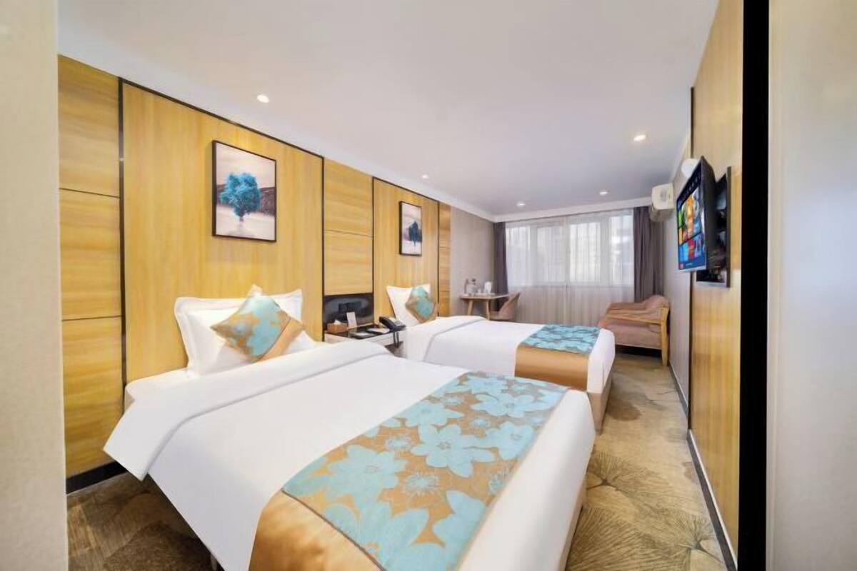 Habitación de hotel con dos camas, un escritorio, una silla, un televisor y una ventana.