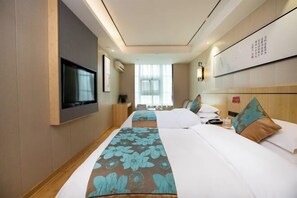 Habitación de hotel con dos camas, un televisor, televisor de pantalla plana montado en la pared y un ventanal con cortinas translúcidas.