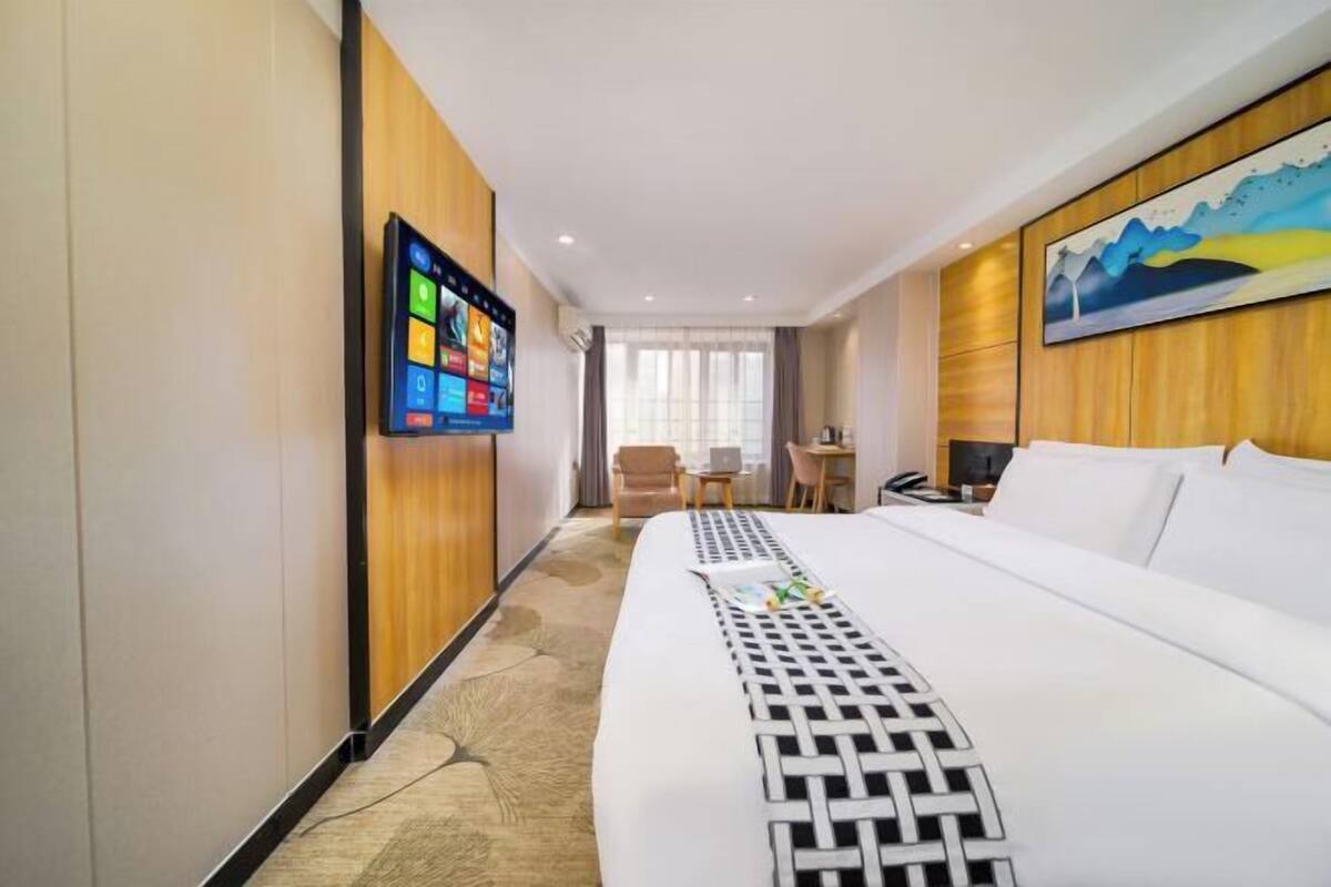 Habitación de hotel con una cama grande, un escritorio, una silla, un televisor montado en la pared y un cuadro colgado.