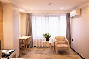 Ett hotellrum med en matplats, en soffa, ett litet bord med en växt och ett fönster med gardiner.
