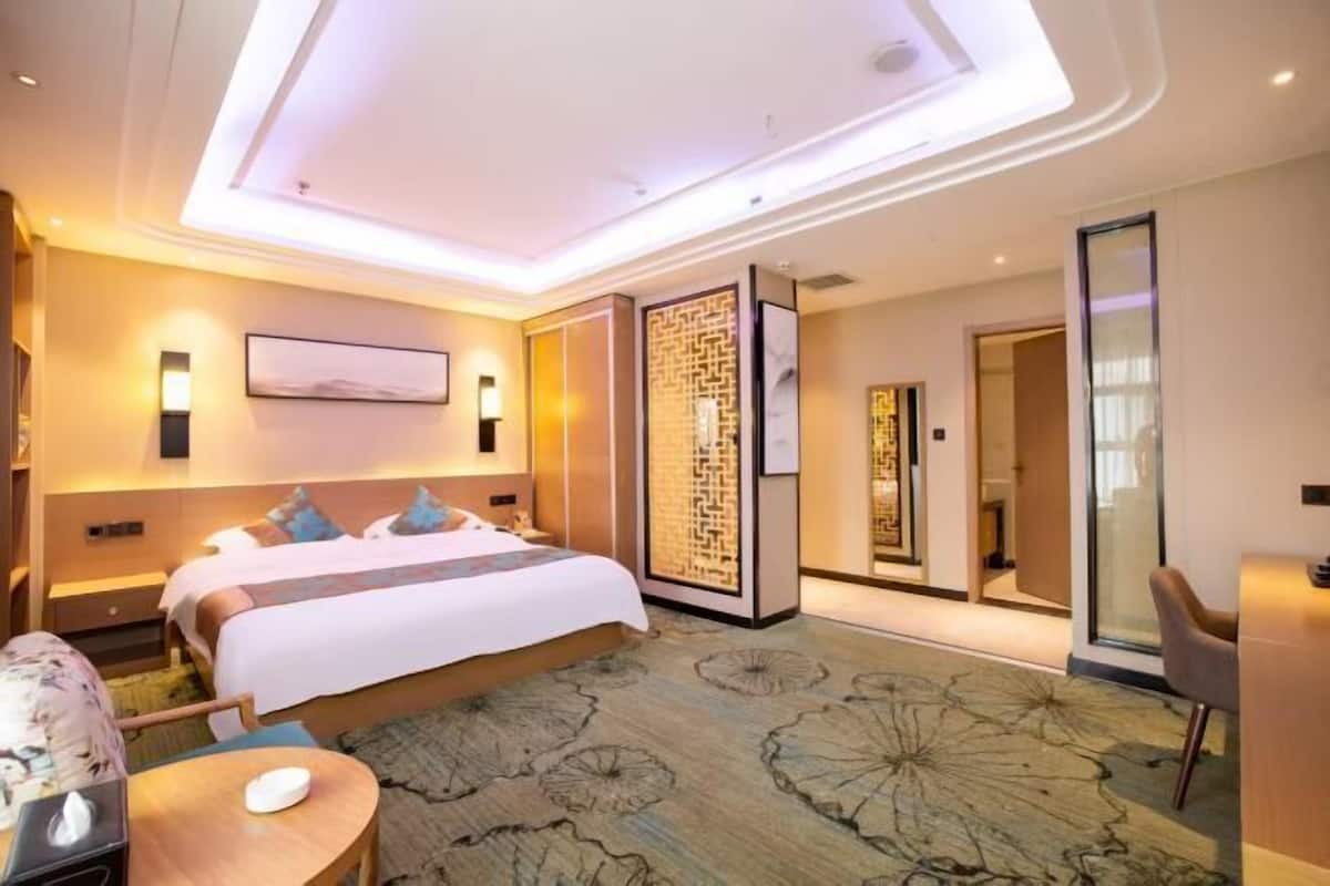 Una habitación de hotel moderna con una cama grande, un escritorio, una silla, un panel decorativo en la pared y vistas al pasillo.