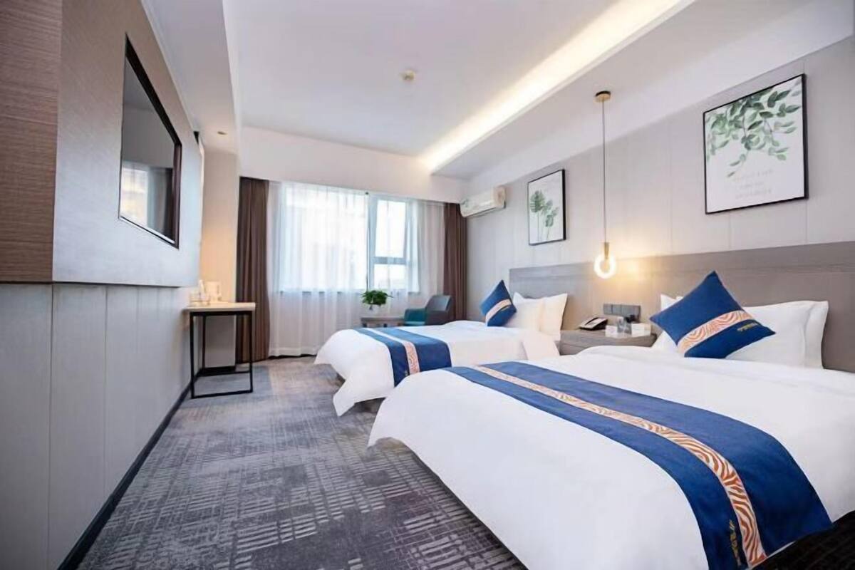 Una habitación de hotel con dos camas, un escritorio, una silla, una mesita de noche y una ventana con cortinas.