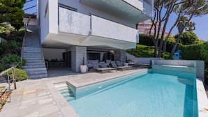 A modern two-story house with a swimming pool, outdoor seating, and a staircase leading to a covered patio.