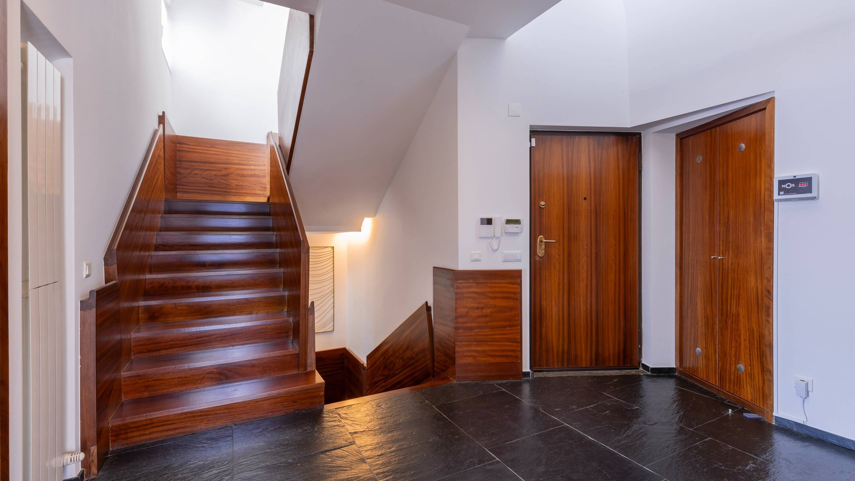 A modern interior with a wooden staircase, a reception desk, and a closed door.