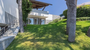 A modern house with a staircase leading to a glass door entrance, surrounded by well-maintained grass and trees.