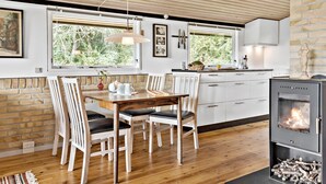 A modern kitchen with a dining area, wooden flooring, white cabinetry, and a wood-burning stove. - 4 bedroom cozy home in Jægerspris (Jægerspris)
