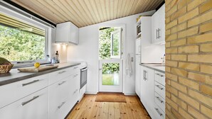 A modern kitchen with white cabinets, a wooden ceiling, and a view of greenery outside. - 4 bedroom cozy home in Jægerspris (Jægerspris)