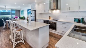 A modern kitchen with white cabinetry, a large island, and a view of the ocean.