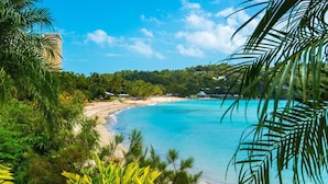 A tropical beach with clear turquoise waters, lush greenery, and a distant building.