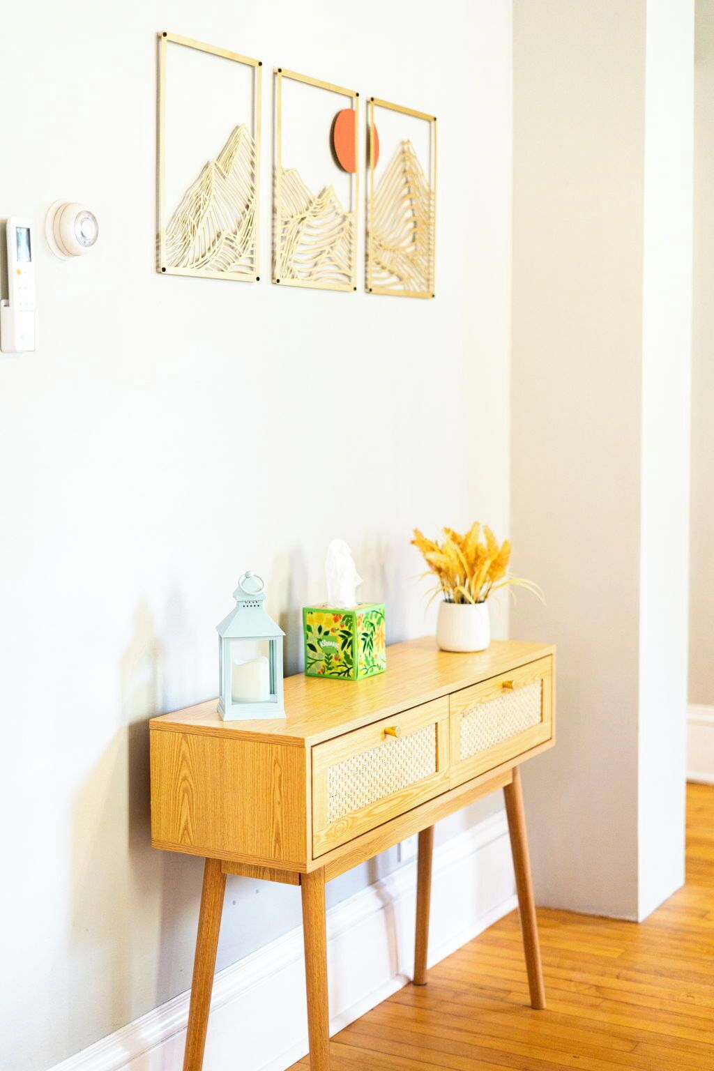 A wooden console table with a tissue box and a lantern, a potted plant, and three framed artworks on the wall.