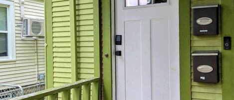 Una casa de color verde con una puerta blanca marcada con el número 2, un buzón y un felpudo.