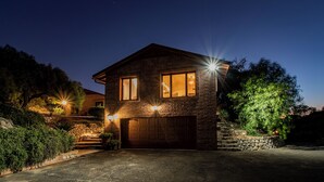 Une maison à deux étages avec une façade en pierre, un garage et une cour avant bien éclairée.