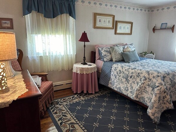 Un dormitorio con cama, mesita de noche, lámpara, ventana con cortinas y alfombra estampada.