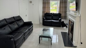 A living room with a black leather sofa, a glass coffee table, a fireplace, and a television mounted on the wall. - 4-bedroom house in charming Lucan with WiFi (Lucan)