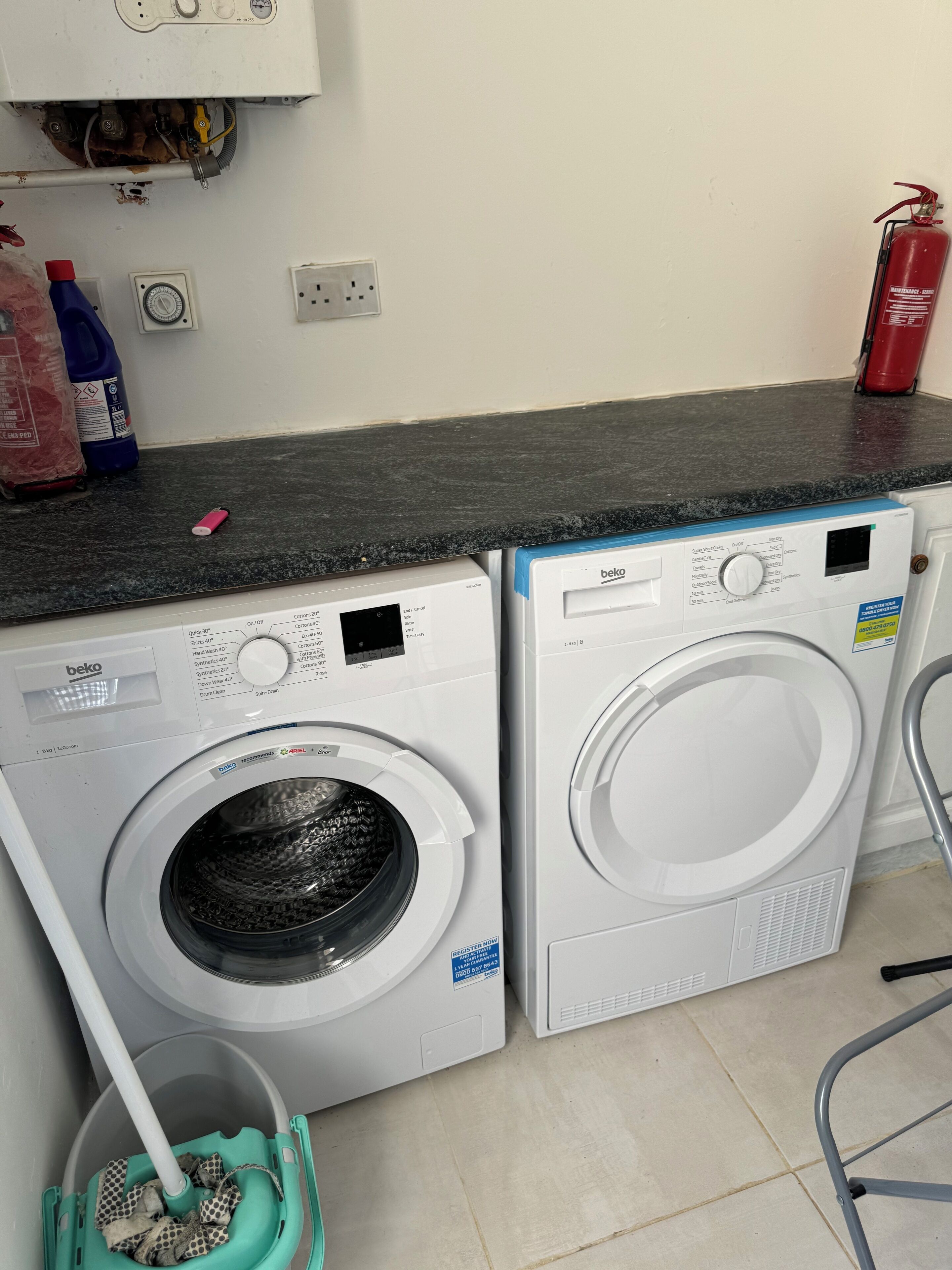 Two front-loading washing machines, a mop bucket, and a fire extinguisher in a laundry room.