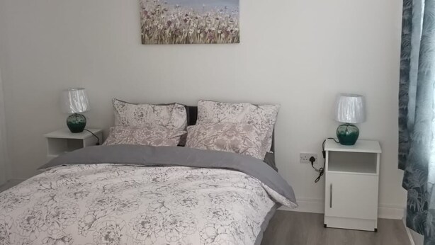 A bedroom with a bed, a nightstand, a lamp, a painting, and a curtain. - 4-bedroom house in charming Lucan with WiFi (Lucan)