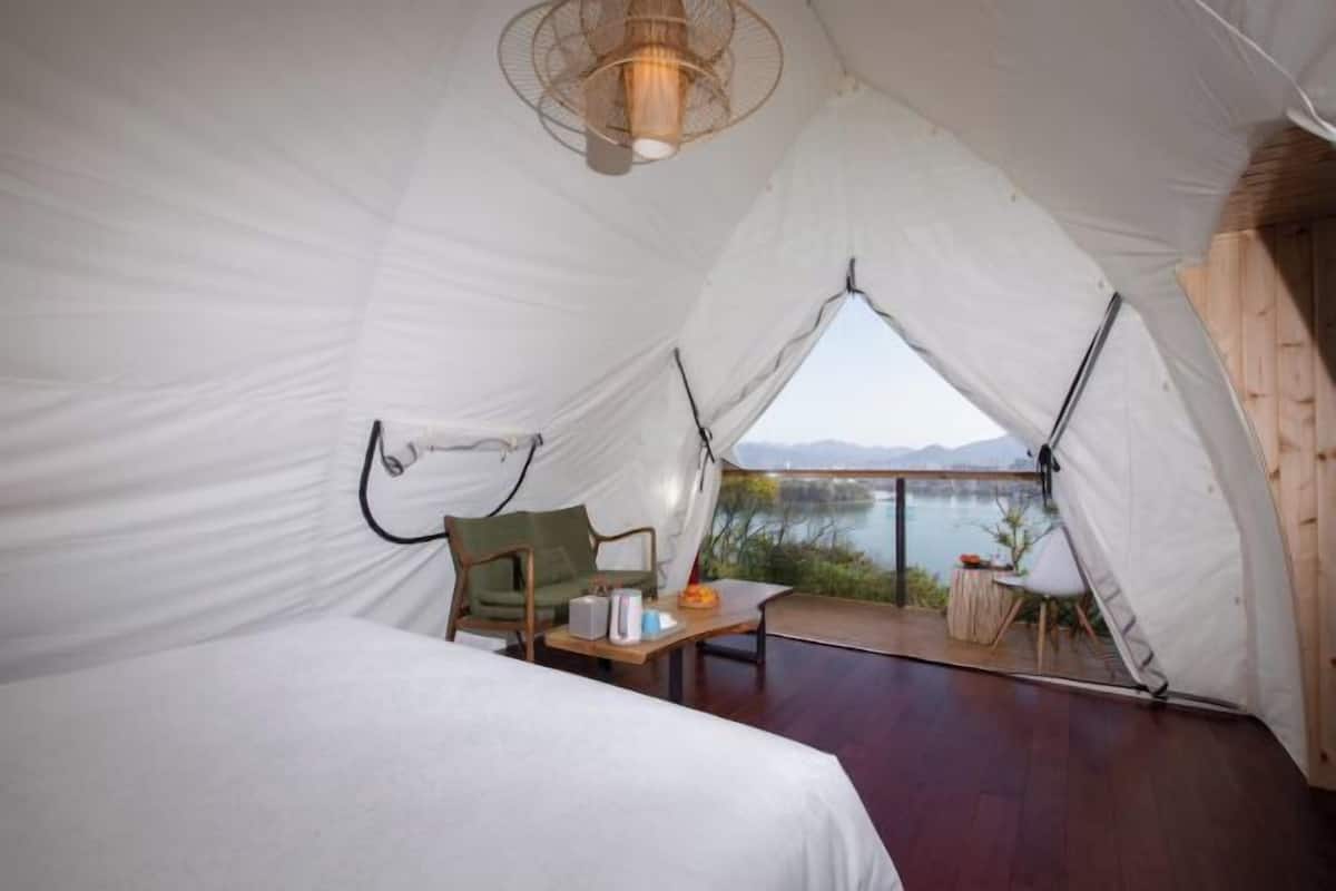 Una carpa con cama, una mesa y una silla, con vista a un cuerpo de agua.