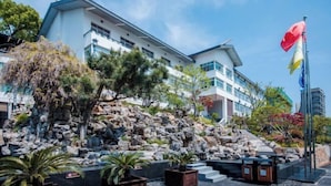 Un hotel moderno con fachada blanca, un jardín rocoso e izado de banderas.
