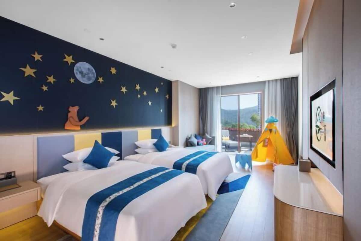 Habitación de hotel con dos camas, un mural del cielo nocturno, un ventanal grande y una tienda de campaña amarilla.