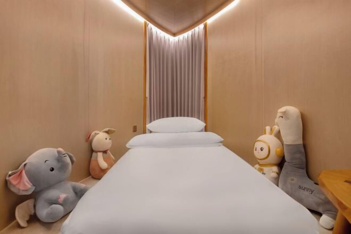 A narrow hotel room with a single bed, a wooden wall, and a curtain.