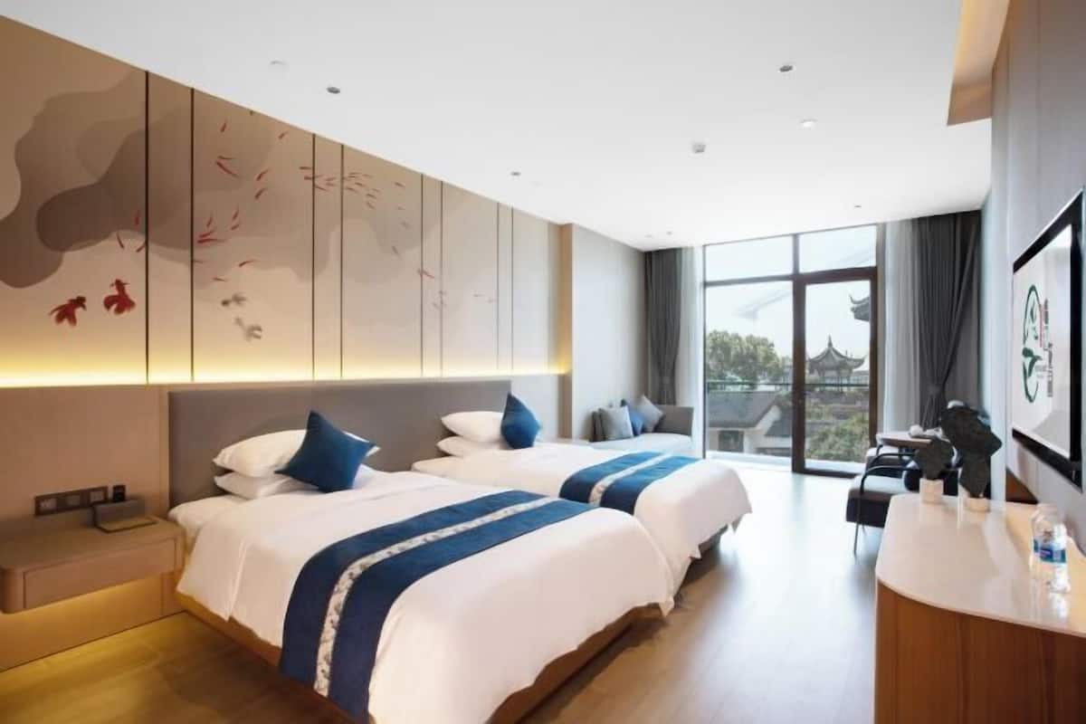 Habitación de hotel con dos camas, un escritorio y un ventanal con vistas a la arquitectura tradicional.