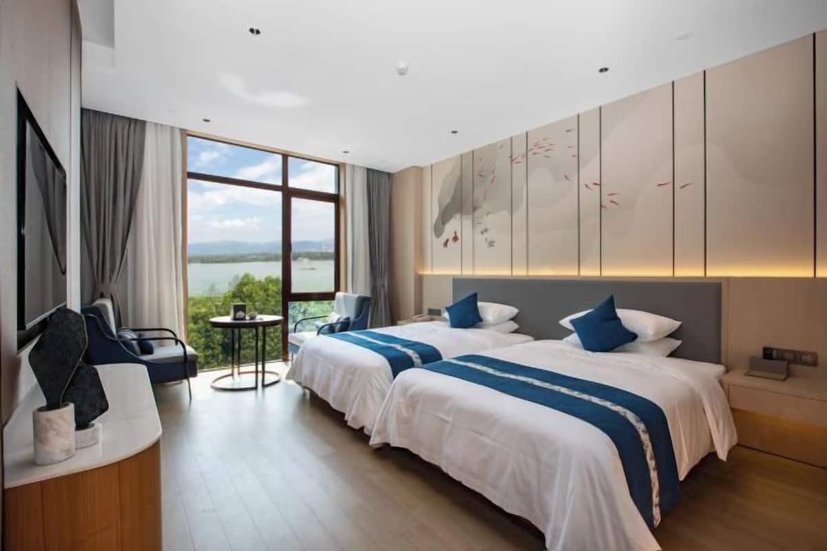 Habitación de hotel moderna con dos camas, un área de descanso y un ventanal con vistas al exterior.