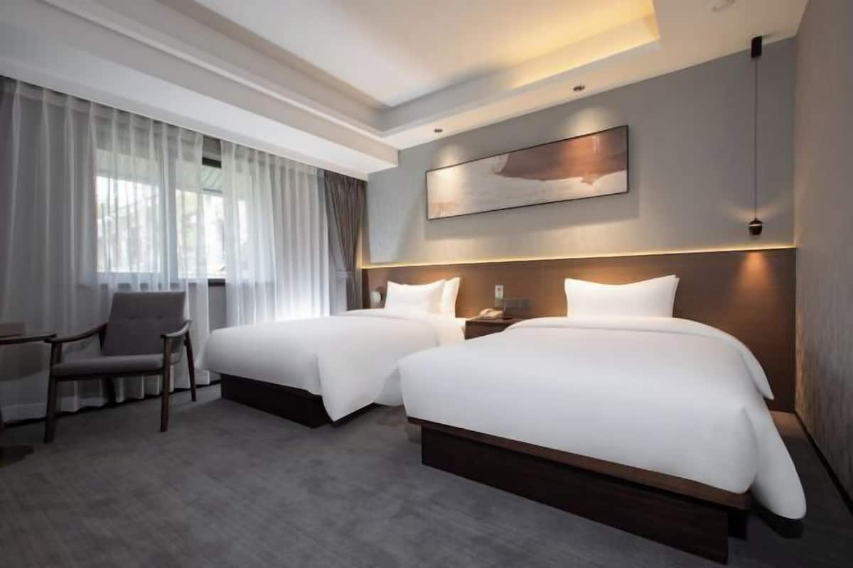 Habitación de hotel con dos camas, una silla, un escritorio y un ventanal con cortinas.