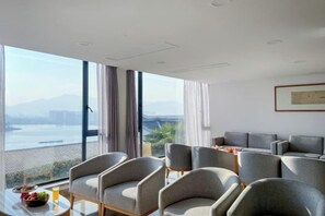Een hotelkamer met een groot raam, een zithoek met stoelen en een tafel met een schaal fruit en een glas.