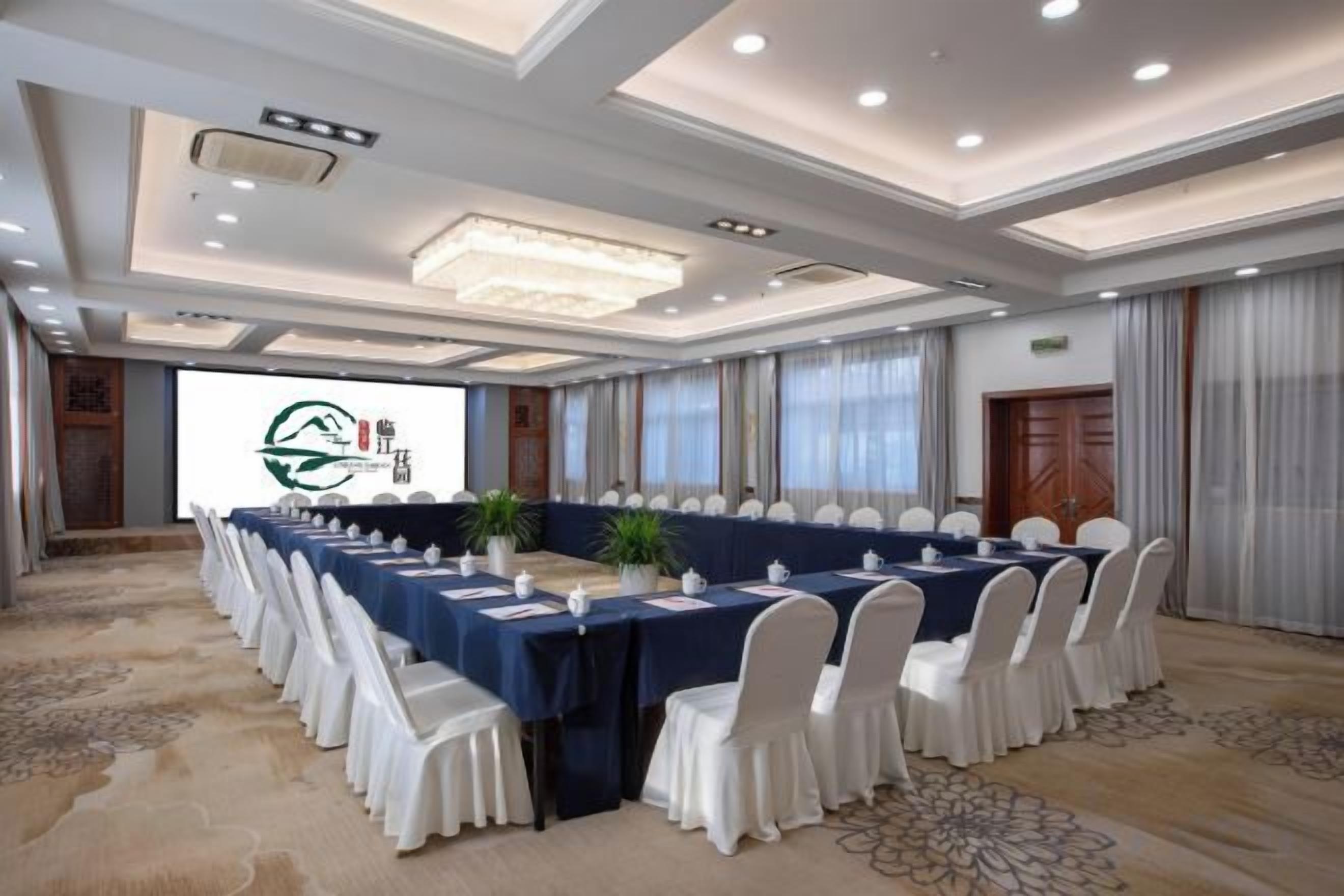 A conference room with a long table, white chairs, and a projector screen.